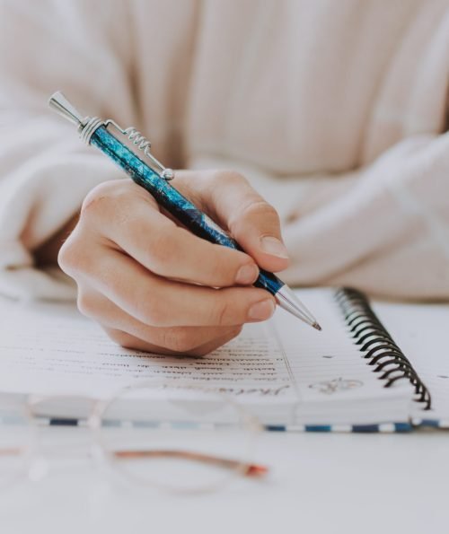 Vertical selective closeup of a female writing in a notebook with a blue pen A vertical selective closeup of a female writing in a notebook with a blue pen